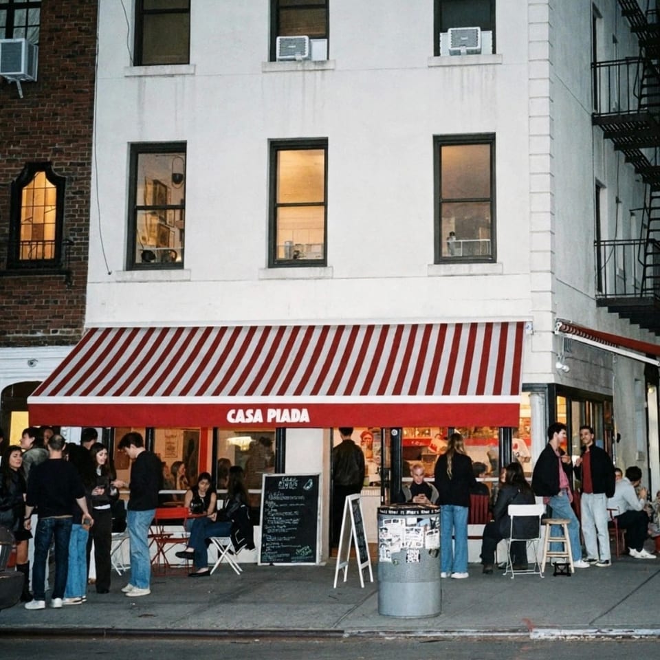 Casa Piada restaurant with a red-and-white striped awning, outdoor seating, and groups of customers on a city sidewalk.
